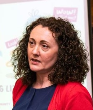 Woman with curly shoulder length hair and a red cardigan speaking at an event