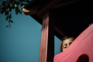 A child peeks from behind a wooden panel in a playground.