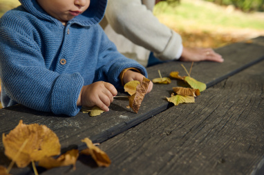 Child playing with leaf at a table outside
