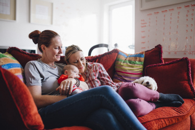 Two women sat on a red sofa with a baby