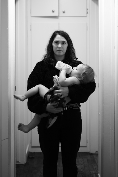 A mother holding her baby stares blankly at the camera.