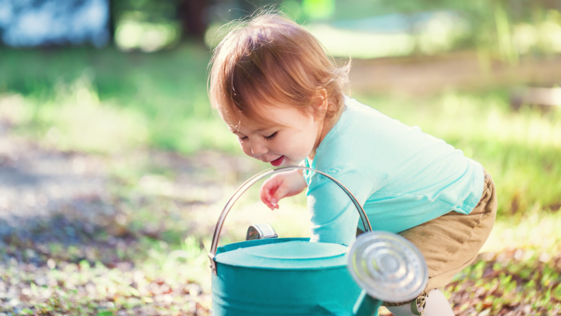 Young child playing with watering can in garden