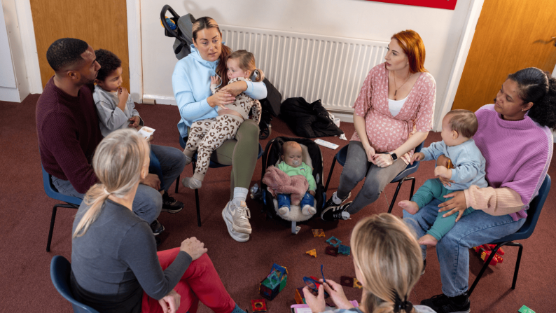 Parents in a group facing each other on chairs with young children on their laps