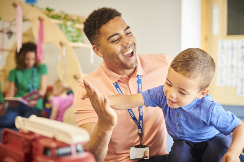 A nursery worker gives a young boy a high five while playing