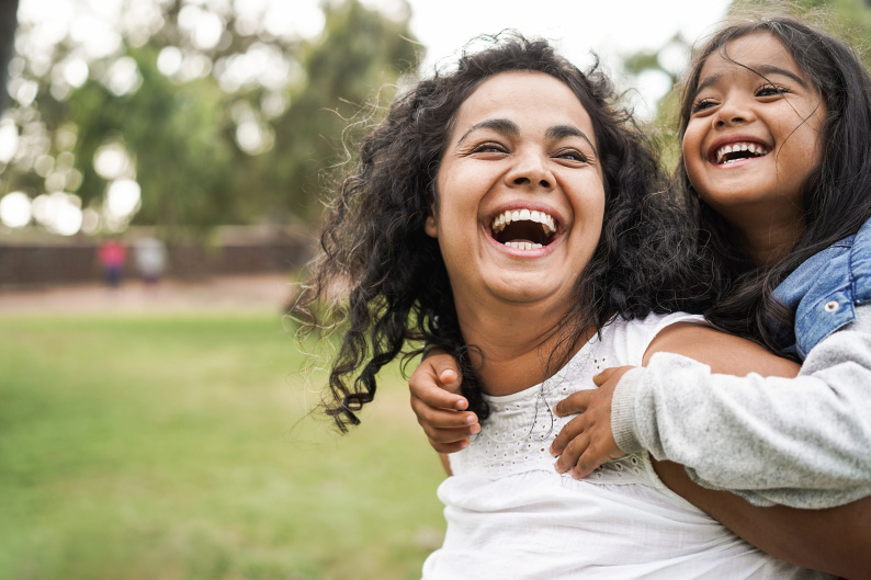 Woman laughing with young girl smiling holding onto her shoulders outside