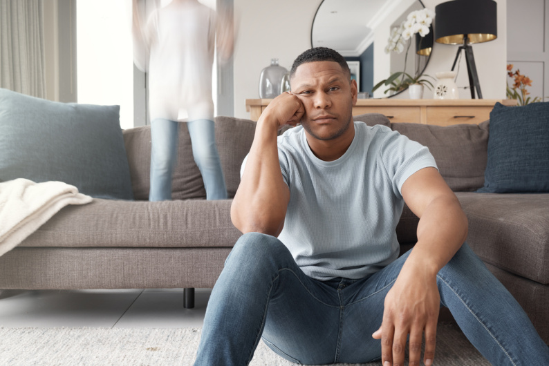 Man sat on the floor looking fed up while child jumps on the sofa behind him