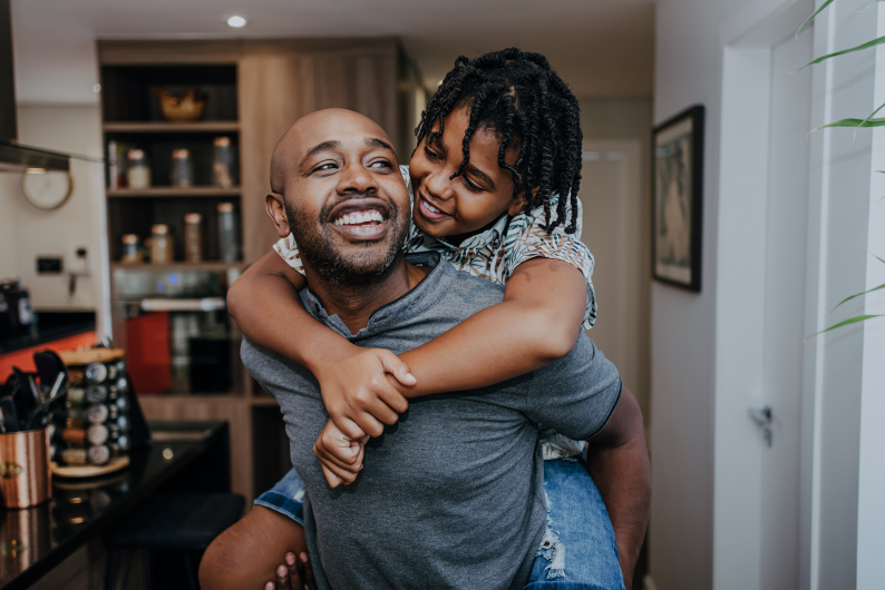 A man smiling giving a child a piggy back