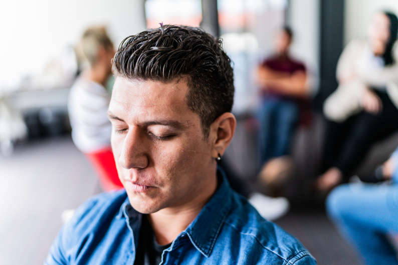 Man with eyes closed with his back to a group behind him