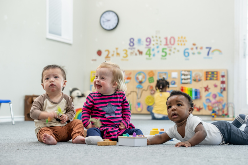Three early years children in a nursery setting, one is lying on his front and the other two are sitting