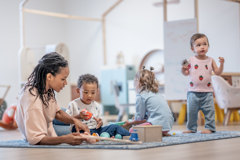 Early years children playing supervised by a woman in a nursery setting