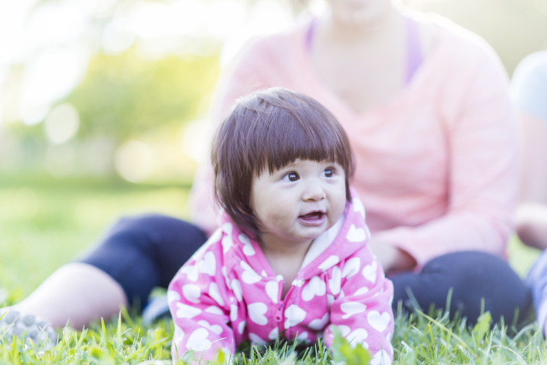 Young girl lying on grass with an adult supervising her sat behind