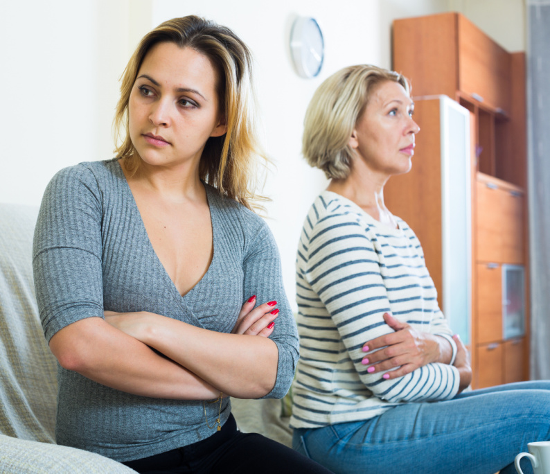 Two women with their arms folded turned away from each other looking annoyed