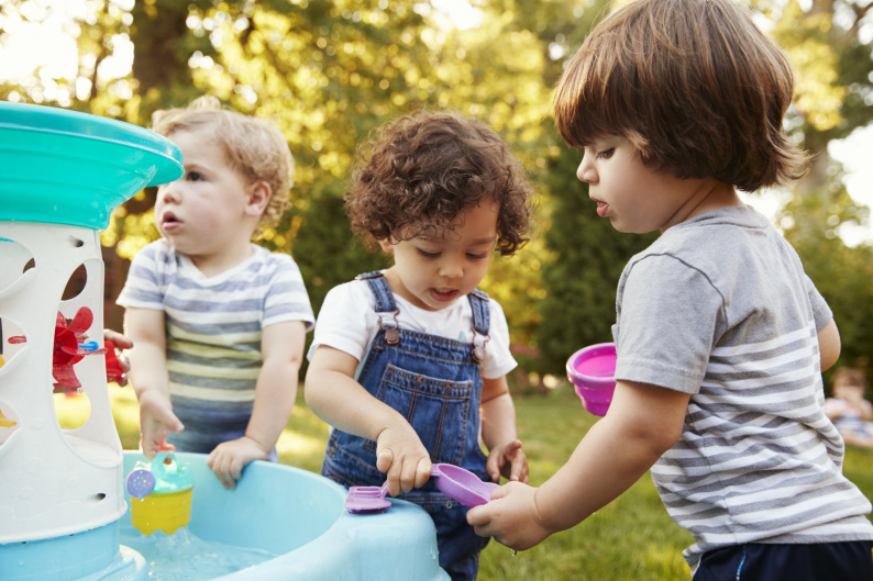 Three young children outside playing with water and bubbles