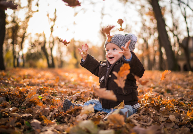 Small child smiling while sat on the floor outside playing with leaves